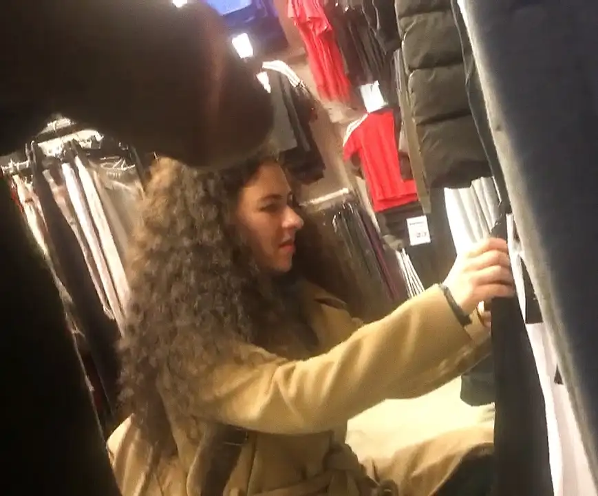 Sexy brunette with curly hair looking at clothes in the store